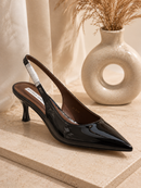 Black high-heeled shoe on a light stone surface with a decorative vase in the background.