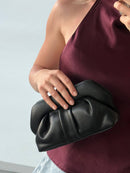 Person holding a black clutch bag against a neutral background