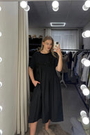 Woman taking a mirror selfie wearing a black dress in a clothing store.