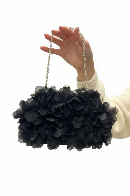 Black floral handbag held by a hand against a white background