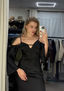 Woman taking a mirror selfie wearing a black dress in a clothing store.