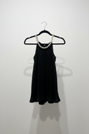 Black top on a hanger with a pearl necklace against a white wall