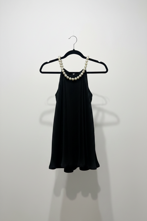 Black top on a hanger with a pearl necklace against a white wall