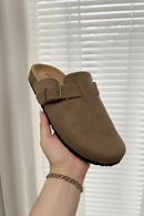 Brown suede clog shoe held by a hand against a neutral background
