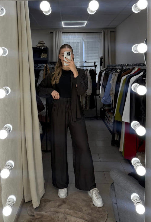 Person taking a mirror selfie in a clothing store with lights around the mirror.
