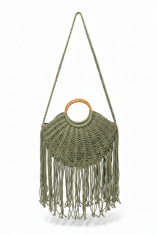 Green macrame handbag with fringe and wooden ring handle on a white background