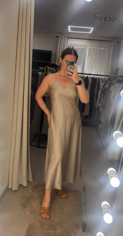 Woman taking a mirror selfie wearing a long dress in a room with a lighted mirror.