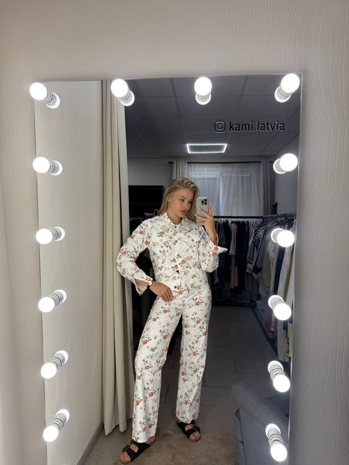 A woman takes a mirror selfie wearing a matching long-sleeve pajama set with a small floral print on a white background. 