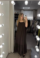 Woman in a long dark dress standing in a clothing store with mirrors and lights.