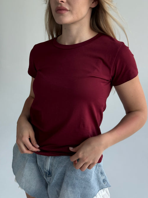 Person wearing a maroon t-shirt and denim shorts against a plain background