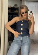 Woman taking a mirror selfie wearing a navy blue strapless top with gold buttons and light blue jeans.