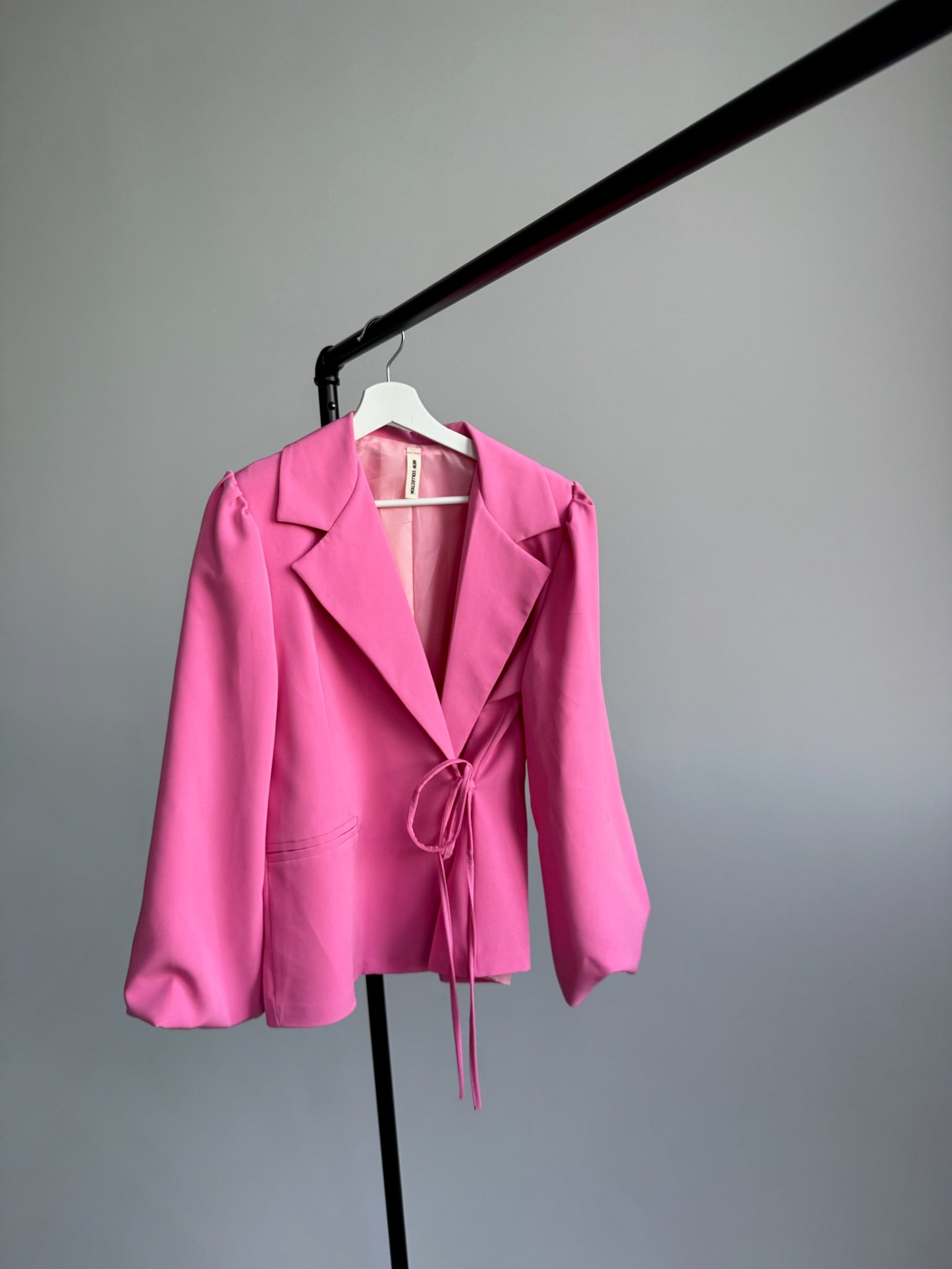 Pink blazer on a hanger against a gray background