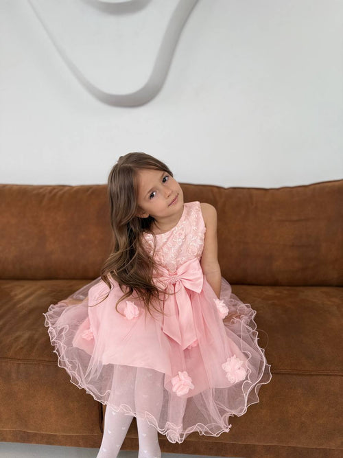 Young girl in a pink dress sitting on a brown couch with a white wall background