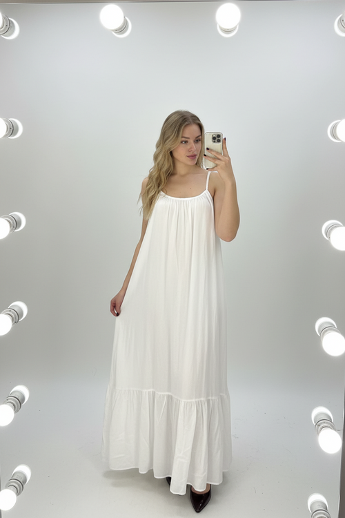 Woman taking a mirror selfie wearing a white dress in a well-lit room.